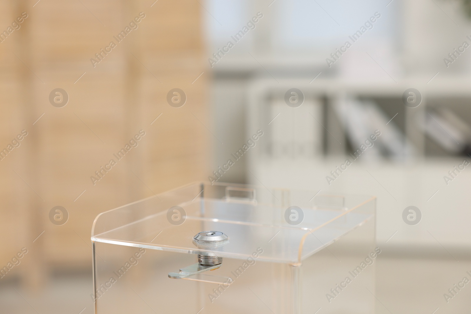 Photo of Transparent ballot box on blurred background, closeup. Space for text