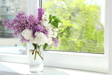 Photo of Beautiful lilac flowers in glass vase on windowsill. Space for text