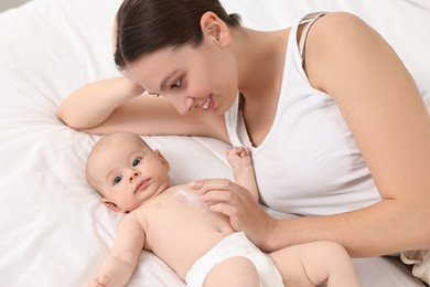 Happy young woman applying body cream onto baby`s skin on bed