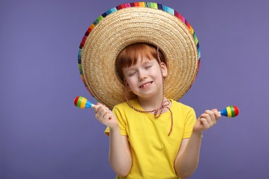 Photo of Cute boy in Mexican sombrero hat with maracas on violet background, space for text