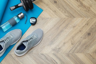 Photo of Exercise mat, ab roller, bottle of water, stopwatch and shoes on wooden floor, flat lay. Space for text