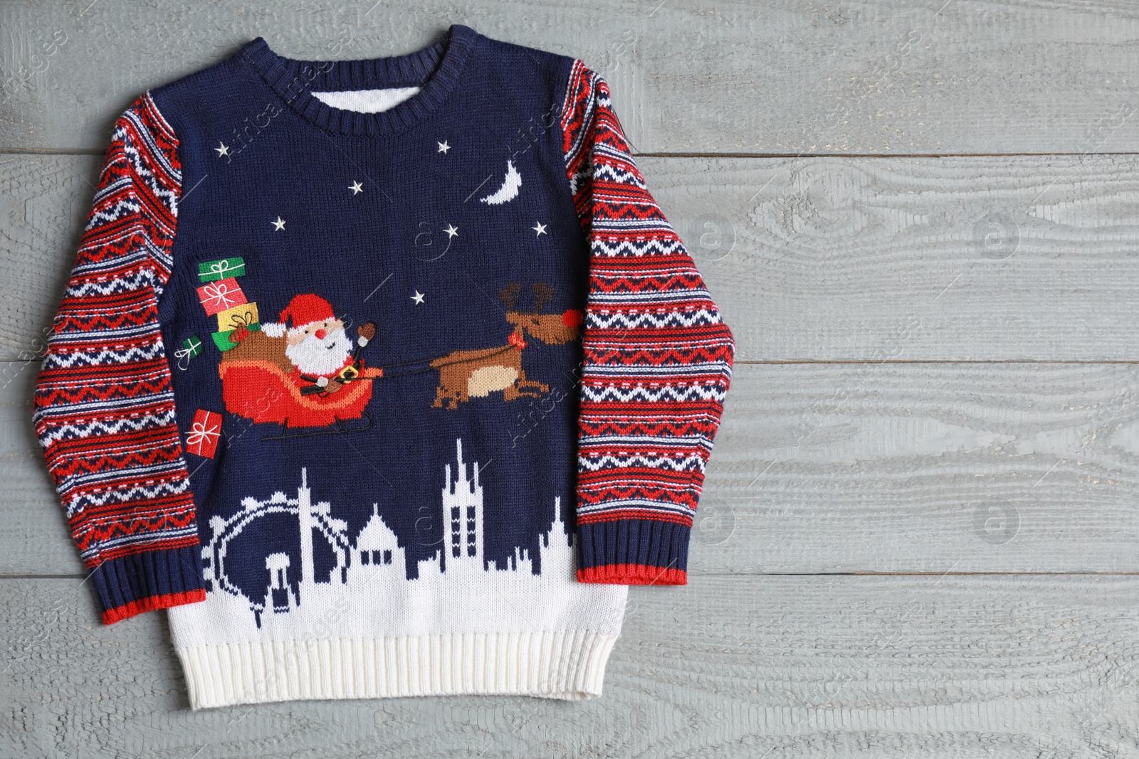 Photo of Warm Christmas sweater on grey wooden table, top view. Space for text