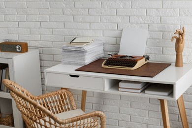 Photo of Comfortable writer's workplace with typewriter on desk near white brick wall