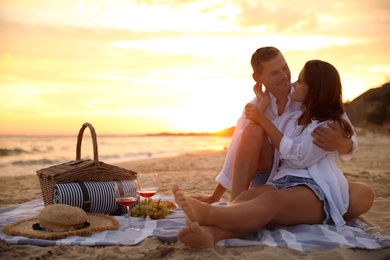 Photo of Lovely couple having romantic picnic on beach at sunset