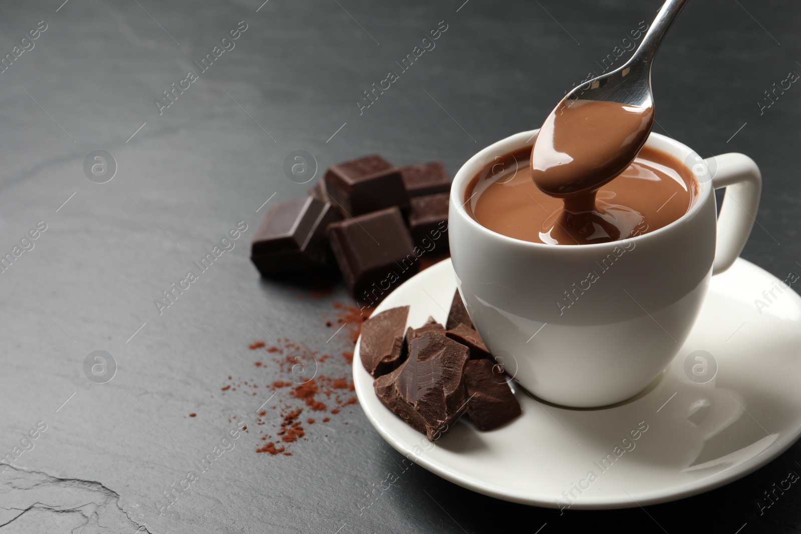 Photo of Spoon with yummy hot chocolate above cup on dark table, space for text