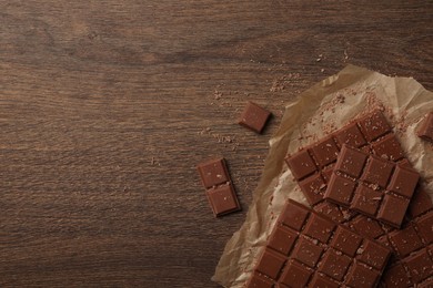 Pieces and crumbs of tasty chocolate bars on wooden table, flat lay. Space for text