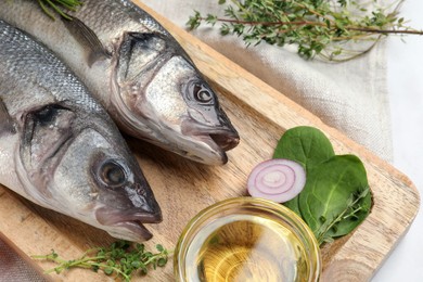 Tasty sea bass fish and ingredients on white table