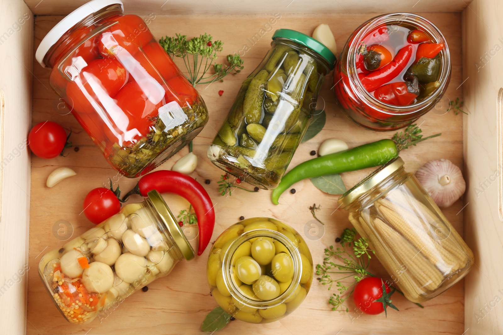 Photo of Jars of pickled vegetables in wooden crate, flat lay