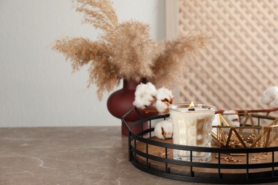 Photo of Burning soy candle with wooden wick near stylish accessories on grey table. Space for text