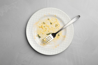 Photo of Dirty plate with food leftovers and fork on grey background, top view