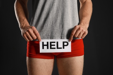 Man holding paper with word HELP on black background, closeup. Urology problems