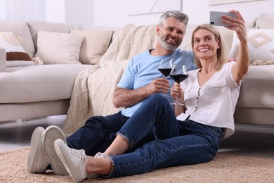 Photo of Happy affectionate couple with glasses of wine taking selfie at home. Romantic date