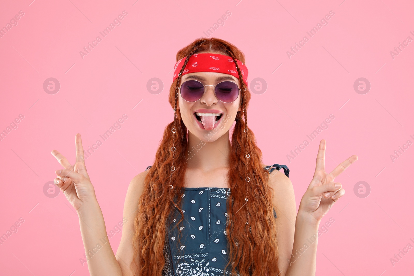 Photo of Stylish young hippie woman in sunglasses showing V-sign on pink background