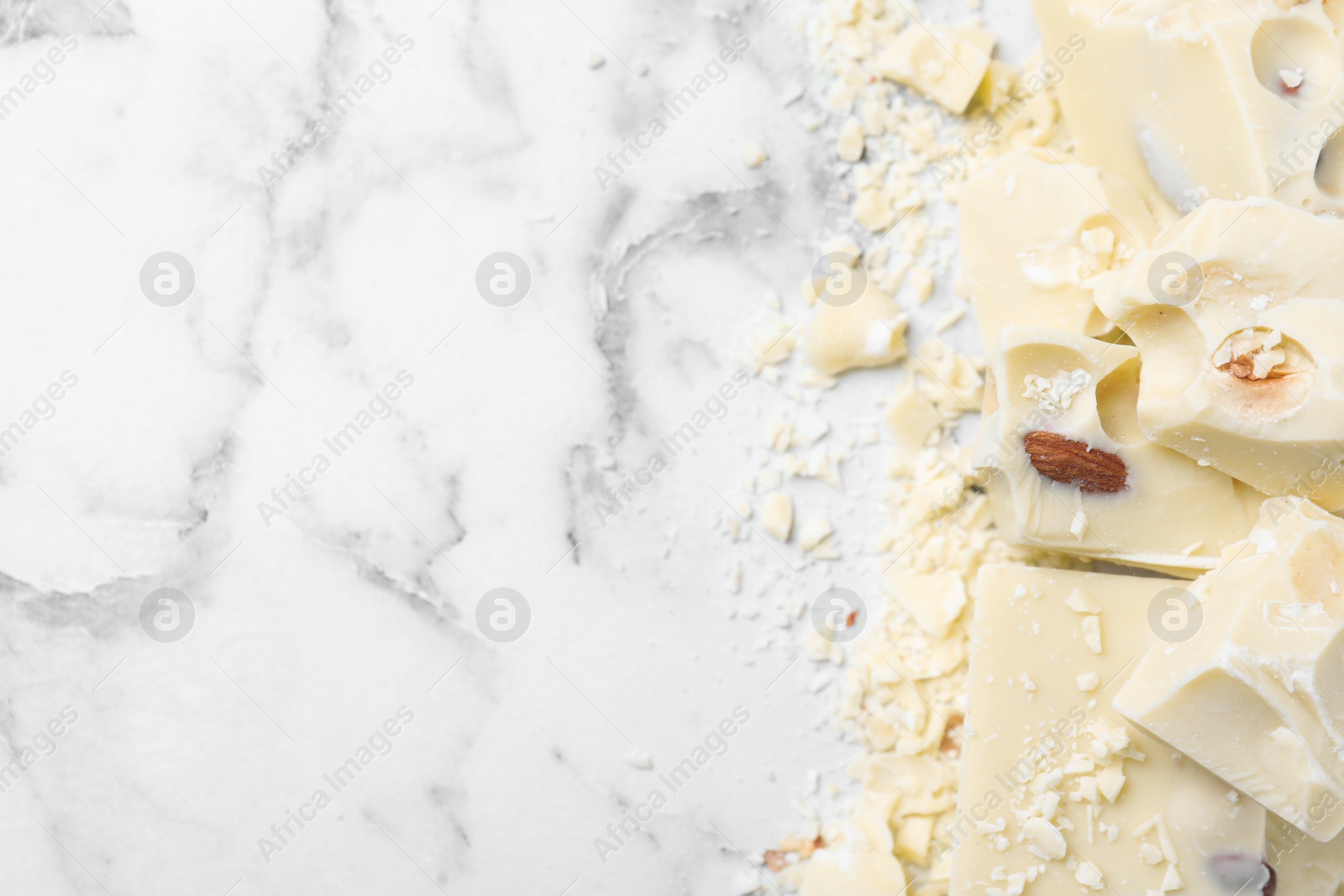 Photo of Pieces of tasty white chocolate with nuts on marble table, flat lay. Space for text