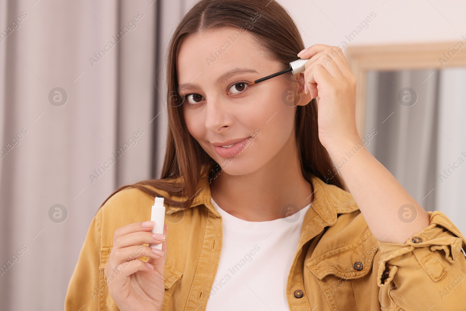 Photo of Beautiful woman applying serum onto eyelashes indoors