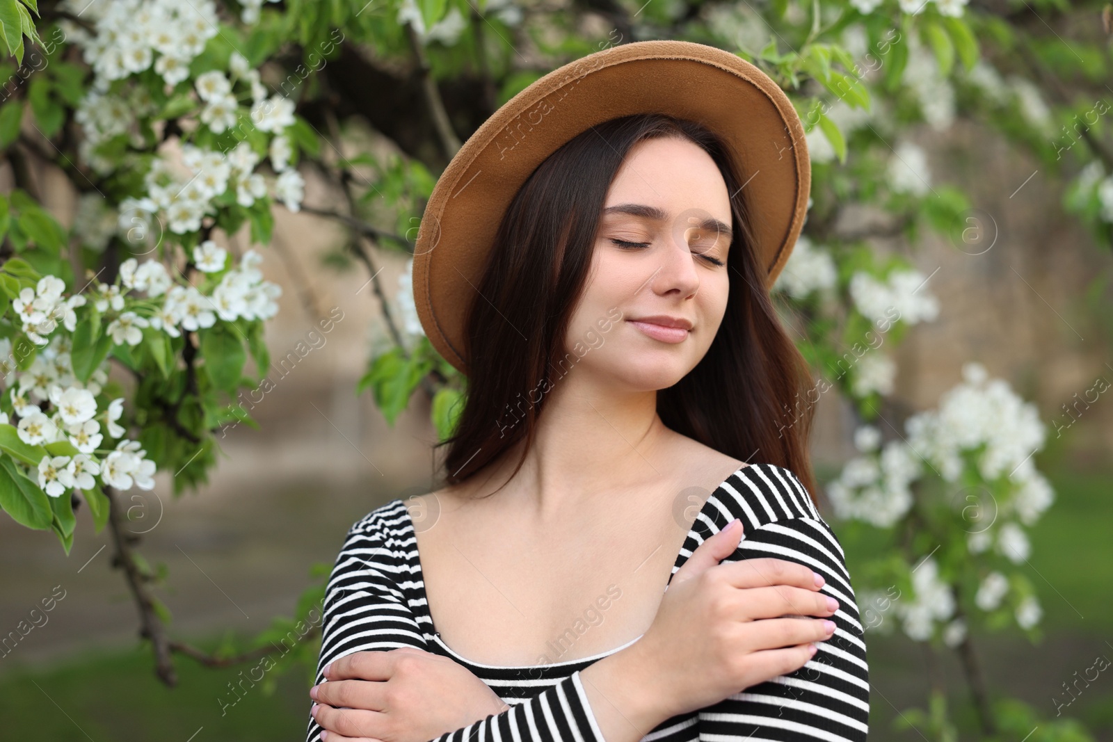 Photo of Beautiful woman in hat near blossoming tree on spring day