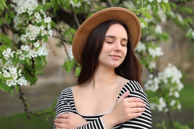 Beautiful woman in hat near blossoming tree on spring day