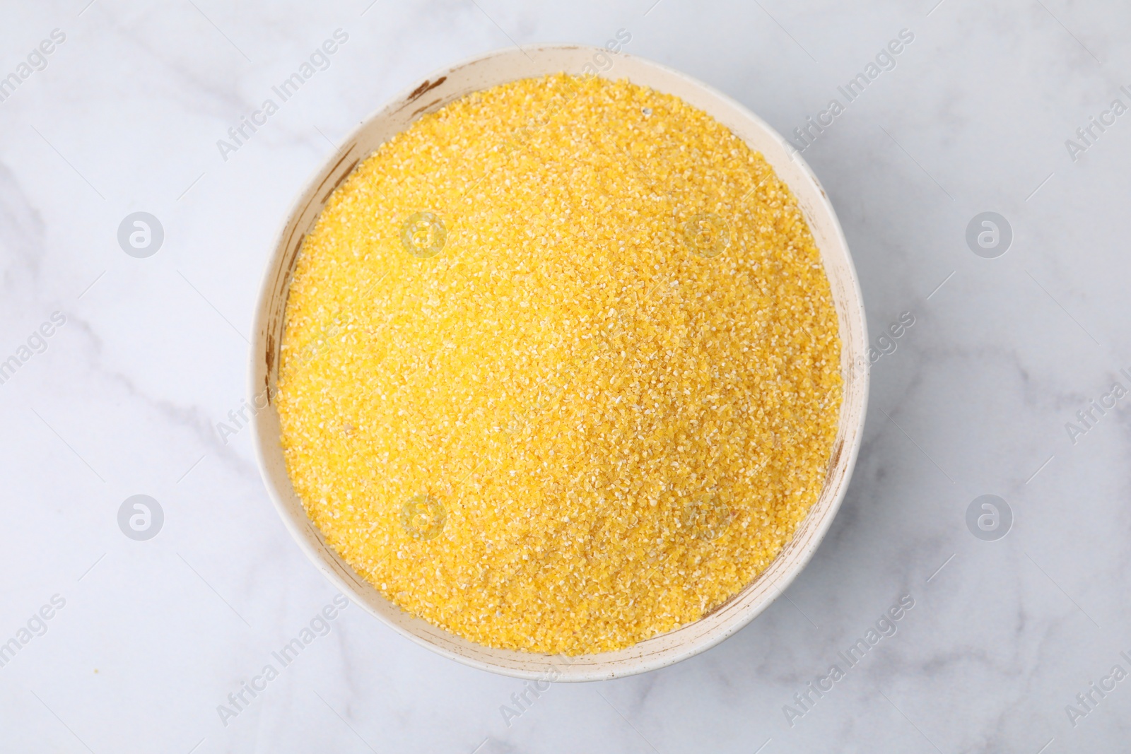 Photo of Raw cornmeal in bowl on white marble table, top view