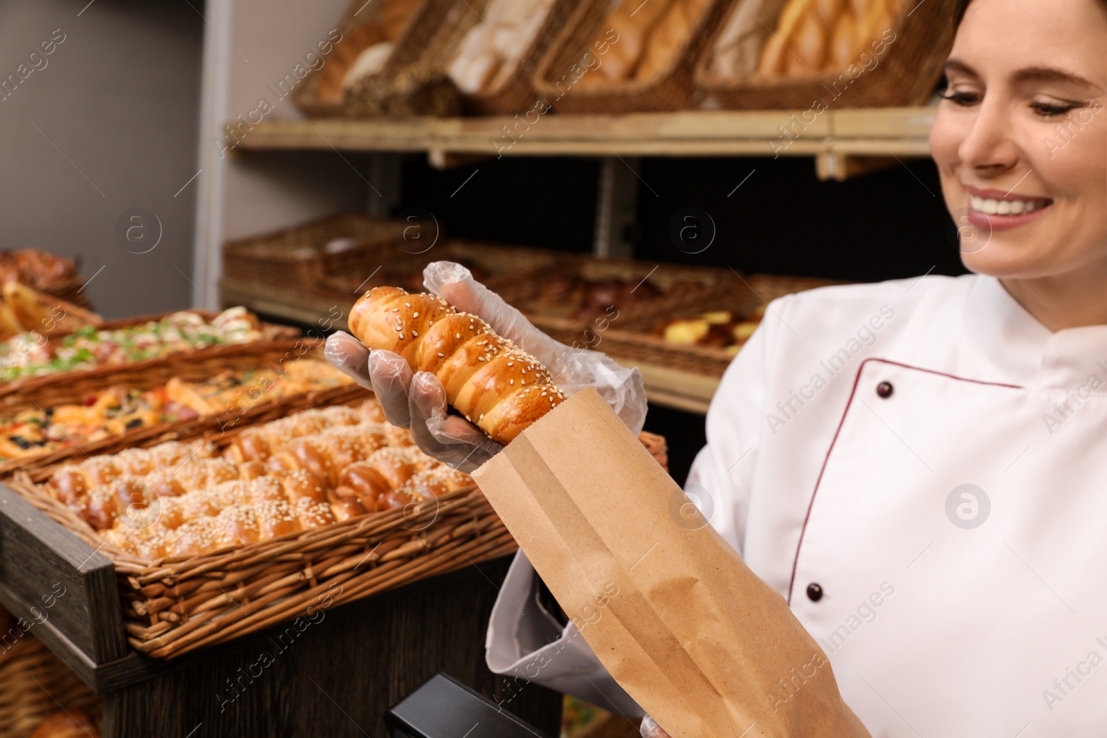 Photo of Baker putting fresh bun into paper bag in store