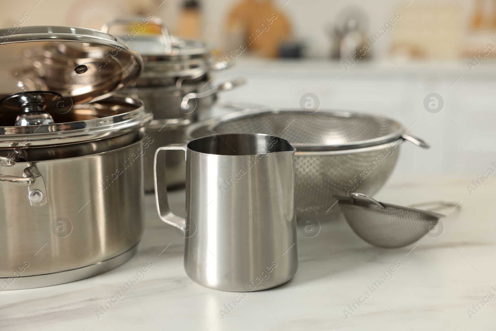 Photo of Set of shiny cooking utensils on white table against blurred background