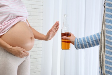 Photo of Pregnant woman declining whiskey indoors. Alcohol harm