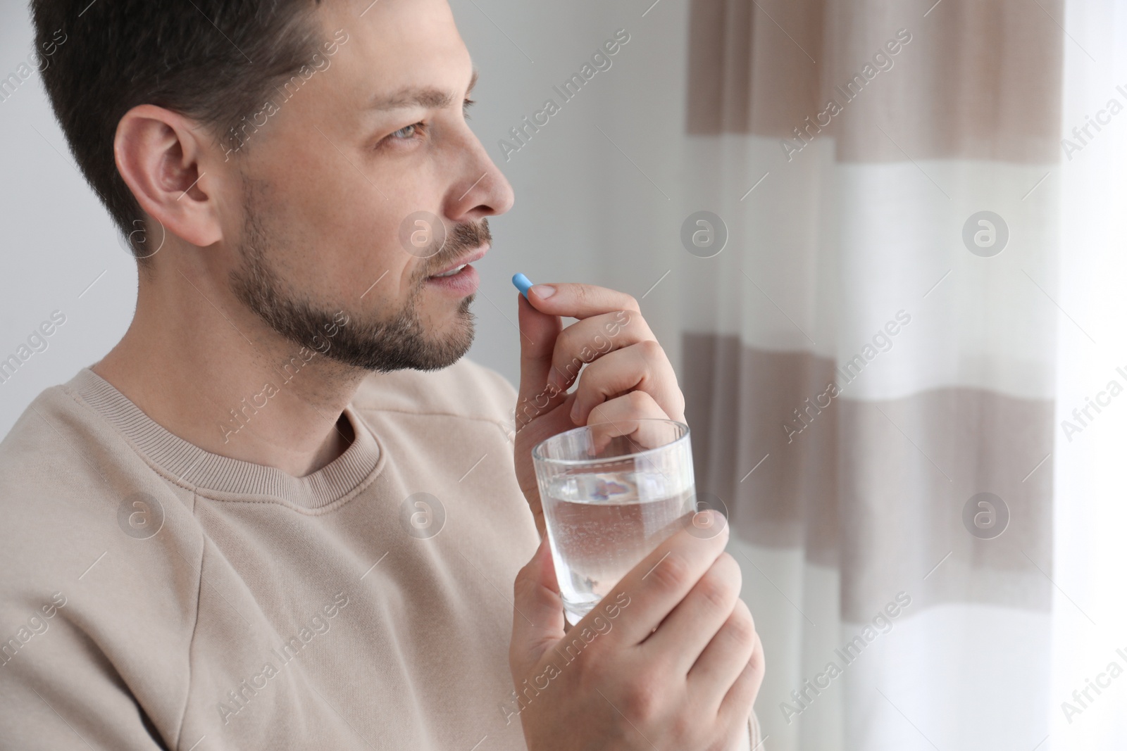 Photo of Man with glass of water taking pill at home