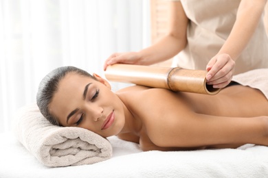 Young woman having massage with bamboo stick in wellness center