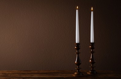 Photo of Elegant candlesticks with burning candles on wooden table. Space for text