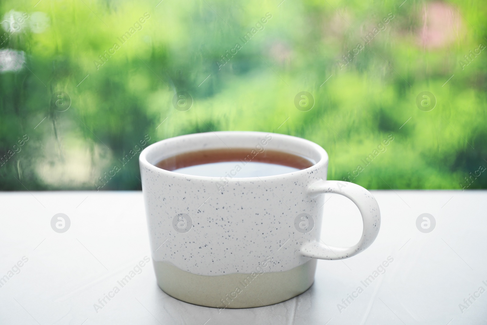 Photo of Cup of hot tea on white windowsill. Rainy weather