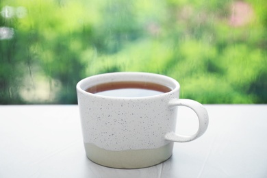 Photo of Cup of hot tea on white windowsill. Rainy weather