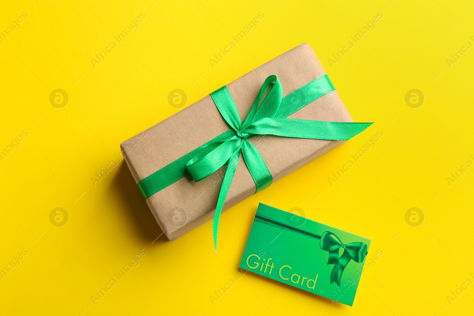 Photo of Gift card and present on yellow background, flat lay
