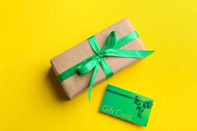 Gift card and present on yellow background, flat lay