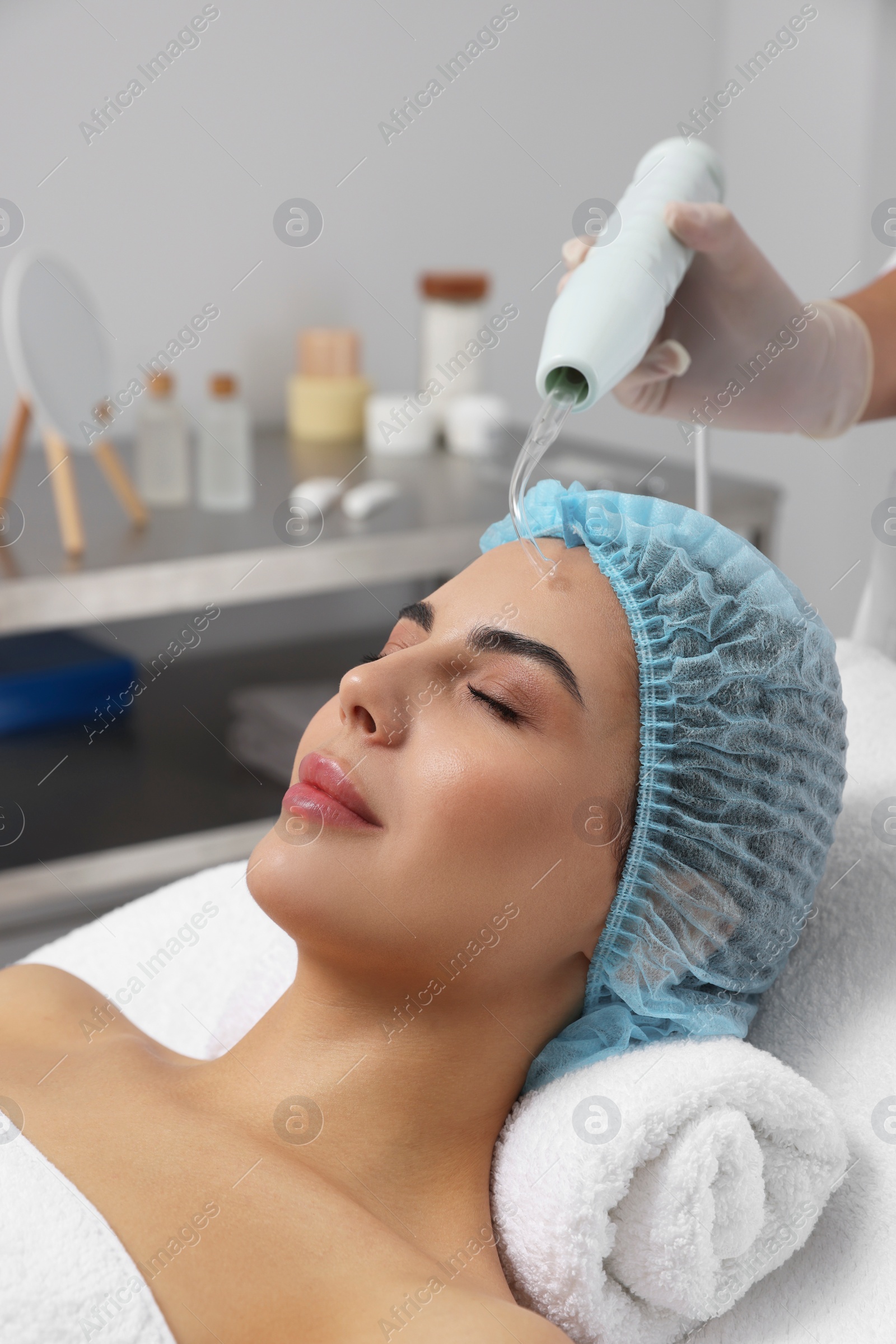 Photo of Young woman undergoing face rejuvenation procedure with darsonval in salon