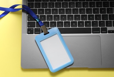 Photo of Blank badge and laptop on yellow background, top view