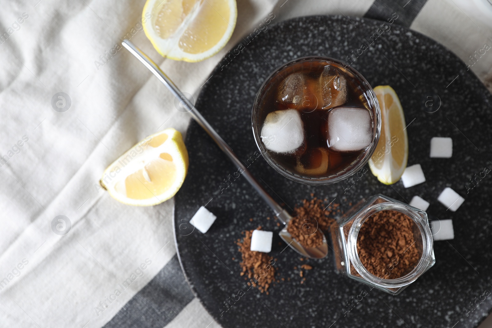 Photo of Refreshing iced coffee in glass, sugar cubes, lemon and spoon on cloth, top view