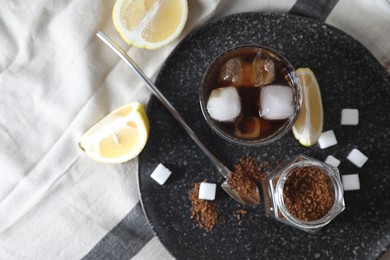 Photo of Refreshing iced coffee in glass, sugar cubes, lemon and spoon on cloth, top view