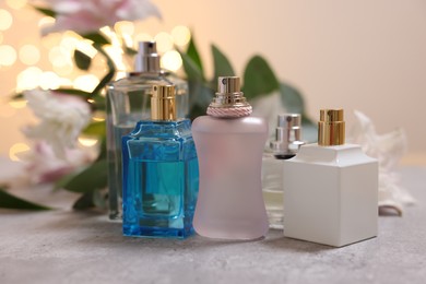 Photo of Perfume bottles and bouquet of beautiful lily flowers on table against beige background with blurred lights, closeup