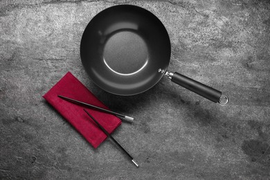 Photo of Empty iron wok and chopsticks on grey table, flat lay