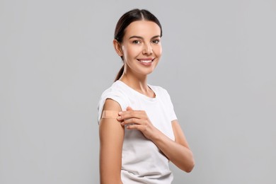 Photo of Woman with sticking plaster on arm after vaccination against light grey background