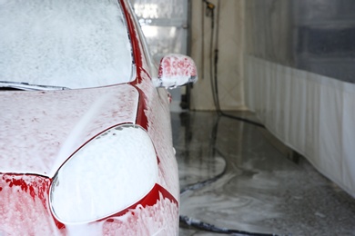 Auto covered with foam at car wash, space for text. Cleaning service