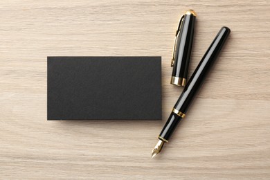 Photo of Blank black business card and fountain pen on wooden table, flat lay. Mockup for design