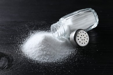 Photo of Organic salt in glass shaker on black wooden table, closeup