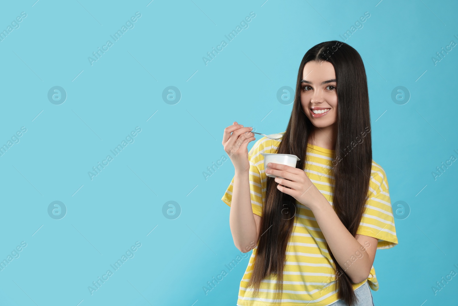 Photo of Happy teenage girl with delicious yogurt and spoon on light blue background. Space for text