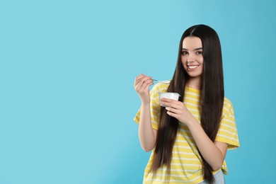 Photo of Happy teenage girl with delicious yogurt and spoon on light blue background. Space for text