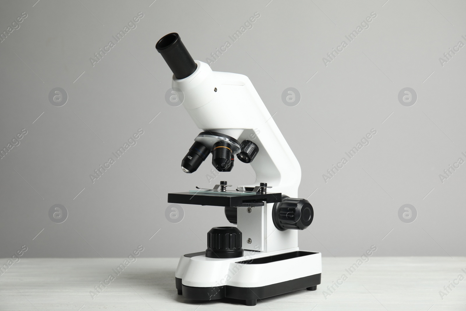 Photo of Modern microscope on white wooden table against grey background. Medical equipment