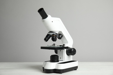 Modern microscope on white wooden table against grey background. Medical equipment