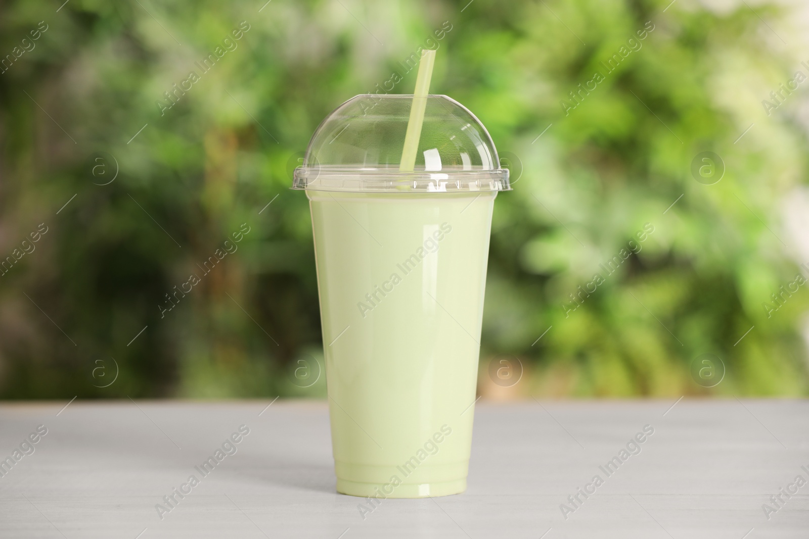 Photo of Plastic cup of tasty smoothie on wooden table outdoors