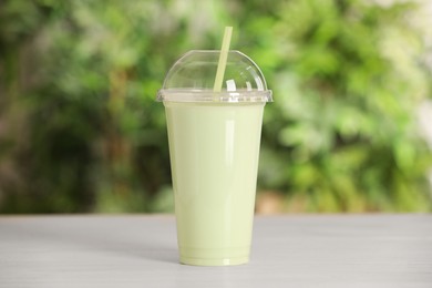 Photo of Plastic cup of tasty smoothie on wooden table outdoors