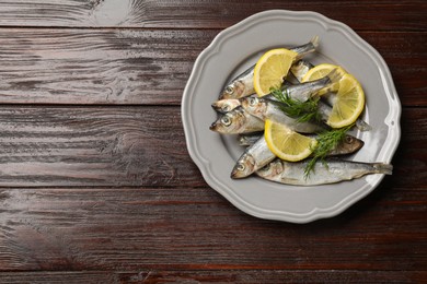 Photo of Fresh raw sprats, dill and cut lemon on wooden table, top view. Space for text