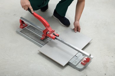 Photo of Worker using manual tile cutter indoors, closeup